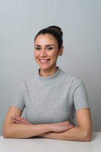 Business headshot of woman in grey sweater in white room